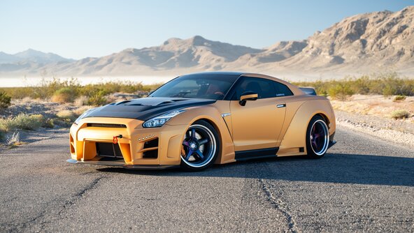 A car is parked on a road in a mountainous, dry rocky landscape. The vehicle is wrapped with high-quality graphic vehicle wrapping from ORAFOL. The high-performance PVC film ORACAL® 970RA Premium Wrapping Cast shimmers in a golden orange colour. | © Source: @orafolamericas